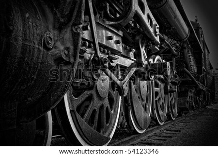 A closeup view of the wheels of an antique steam train, in black and white.
