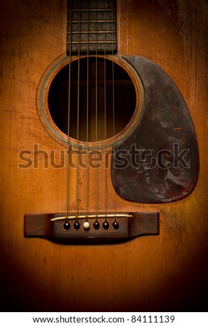 A close-up image of the sound-hole, strings and bridge of a very old, vintage, scratched and beat-up acoustic guitar.
