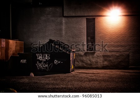 A dirty, dark, shadowy and dangerous looking urban back-alley at night time with garbage dumpster.
