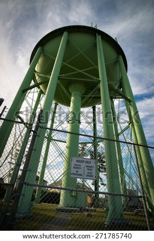 A giant, green public water tower looms tall overheard with \'keep out\' sign in the foreground.