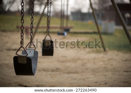 Children\'s swings hang empty an idle at a playground on a dull, overcast day.