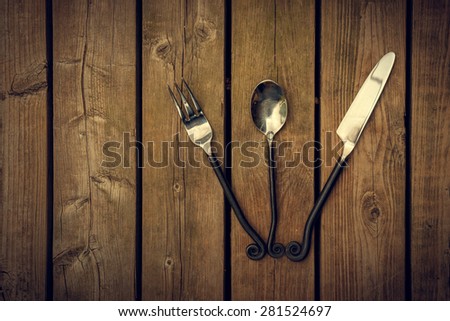 Vintage antique style cutlery, a fork, spoon and knife with twirled design metal stems fanned out on a natural wooden board background.