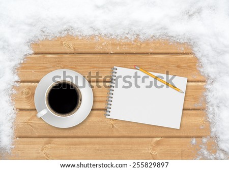 A cup of coffee, a pencil and a notebook, viewed from the top, on the planks covered with snow