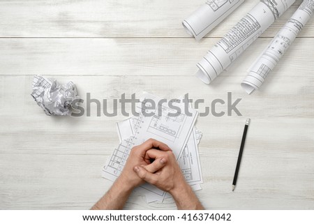 Closeup masculine folded hands on wooden panel with hand-folding a piece of paper. Worry process. Top view composition. Anger sign. Workplace of architect or constructor. Engineering work
