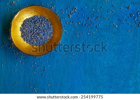 Lavender seeds in handmade coconut bowl decorate with gold from the inside on blue wooden background. Top view. Space for text.