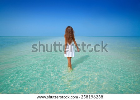 Beautiful girl in white dress walk on the water on tropic beach in Phangan