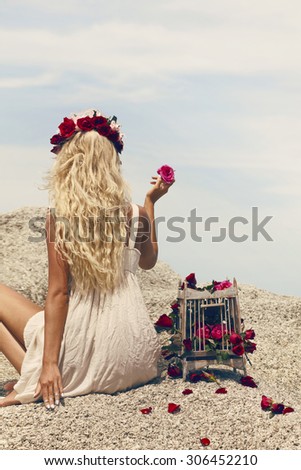 Retro vintage style image of beautiful blonde woman with bird cage full of red roses.