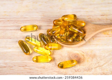 Closeup the yellow soft gelatin supplement fish oil capsule on wooden plate