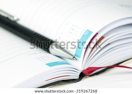 selective focus of the ball pen on opened lined diary book with calendar page