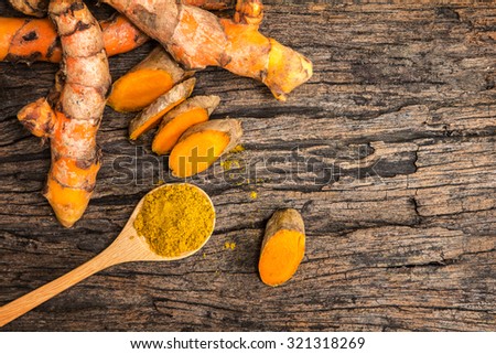 the turmeric powder in spoon and roots on wooden plate