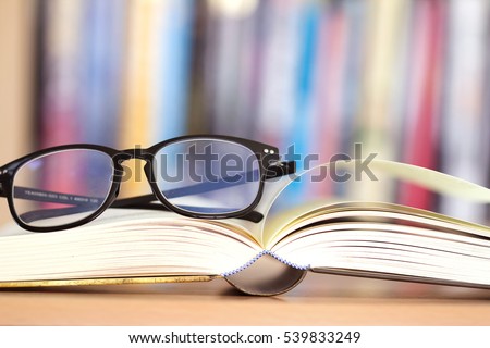 Close up opened book page and  reading eyeglasses with  blurry bookshelf background for education and publication concept , extremely shallow DOF