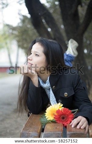 Girl with flowers laying on the bench in autumn park, dreams