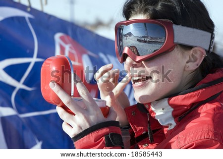 Attractive sport girl snowboarder applying face pack outdoors in winter mountain