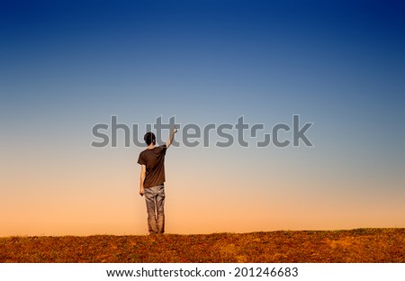man alone pointing to the sky in an empty landscape at dusk