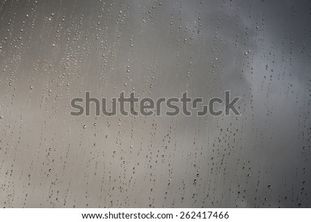 shinny rain droplets on a window, dark clouds in the background
