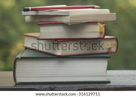 pile of old books, note pad and pencil on a garden wooden table