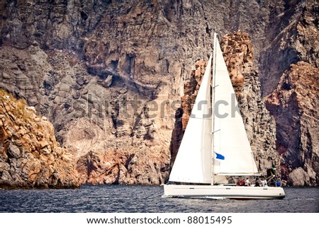 Sailing ship yacht with white sail in open sea. Rocks in the background