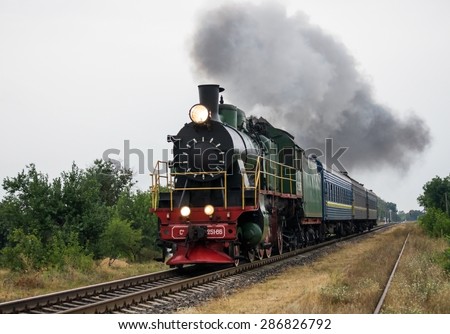 Old steam locomotive travels by rail and produces smoke
