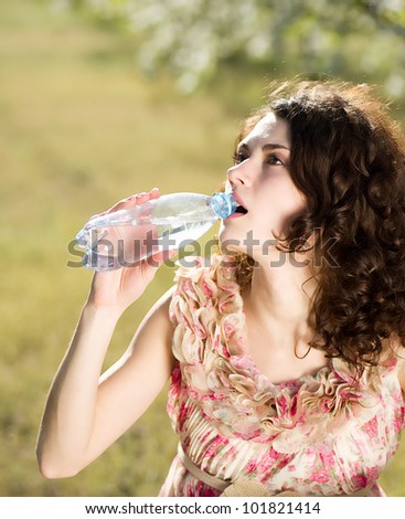 Beautiful woman drinks cold water in spring garden