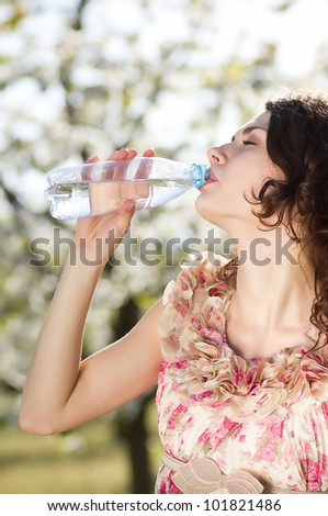 Beautiful woman drinks cold water in spring garden