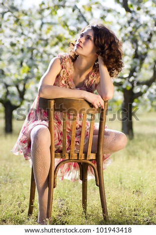 Beautiful woman sits on a chair in a spring garden
