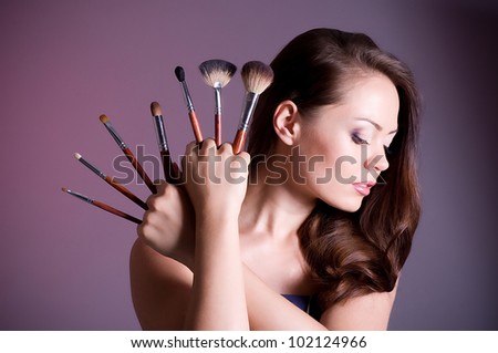 Beautiful woman applying makeup on face on dark background