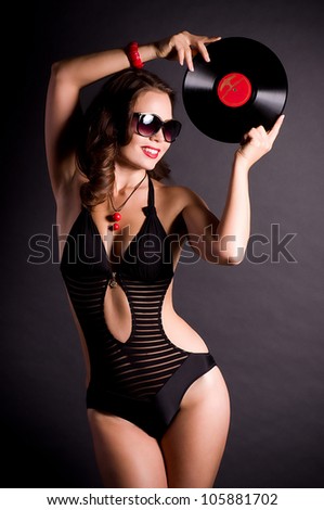 Sexy young woman in retro style with vinyl plate on black background.