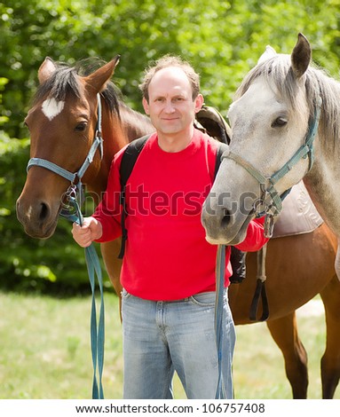 Handsome smiling man with horses in the forest