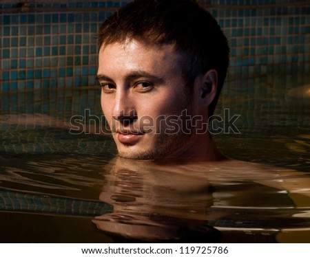 Young wet sexy muscular man posing in the swimming pool