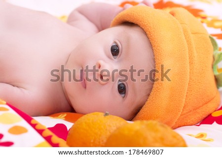 Newborn baby girl in orange hat with mandarin