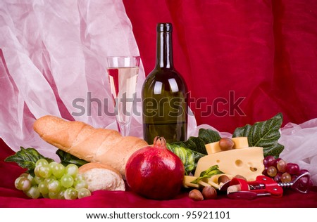 Beautiful composition with wine, grape, cheese, pomegranate and long loaf on red background