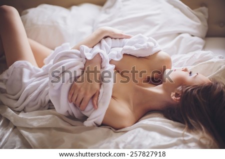 Beautiful young woman in white bathrobe in bedroom at home