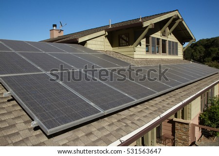 solar panels on roof of house. horizontal orientation, blue sky, gray panels on brown roof.