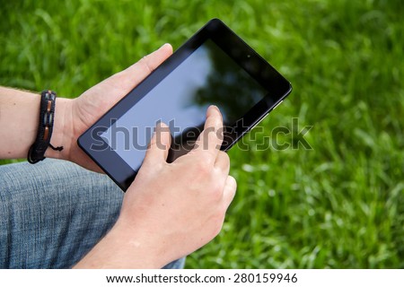 Businessman holding and touching on touch screen digital tablet in the park. Background green grass