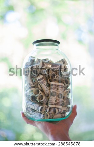 Hand holds a glass jar full of money on blurred background