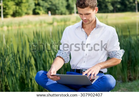 Escaped of office. Business style dressed man sitting in the park working on laptop and green terrace on background