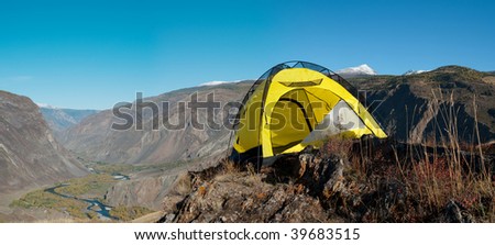 Mountain canyon panorama with yellow tourist tent stands on the brink of a precipice
