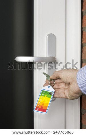 Energy label on key in mens hand unlocking a front door of a new home
