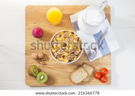 A varied breakfast on wood table with a belly pitcher of milk, a bowl with cornflakes, orange juice, kiwis, two toast, walnuts and a plum (zenith photo)