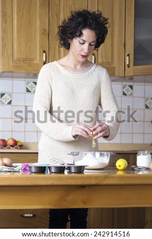 Young woman breaking an egg making cupcakes. Modern housewife cooking homemade traditional cupcakes in a rustic kitchen
