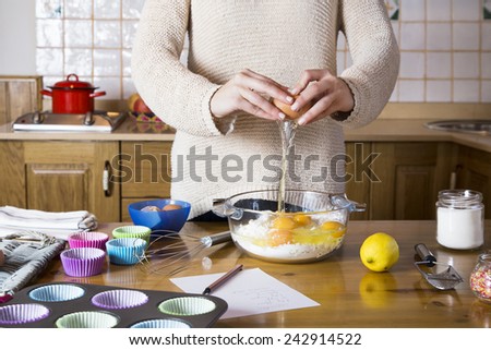 Woman hands breaking an egg to make cupcakes. Woman cooking homemade traditional cupcakes in a rustic kitchen