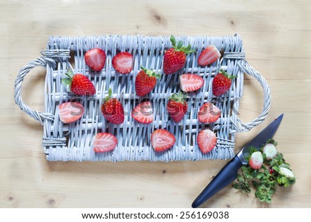 Fresh strawberry on a wicker tray and the rests with knife over a rustic wood background (desk). Top view. Cut and whole strawberries on wooden table