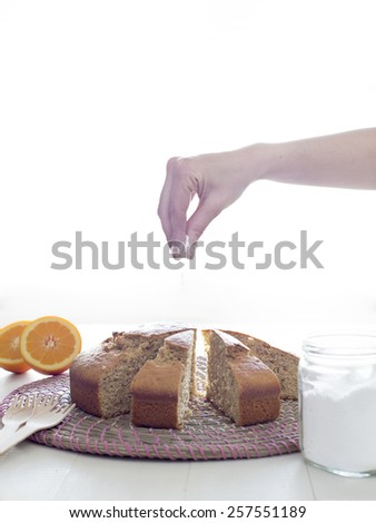 Pouring icing sugar over cake. Human hand sprinkling powdered sugar over sponge cake