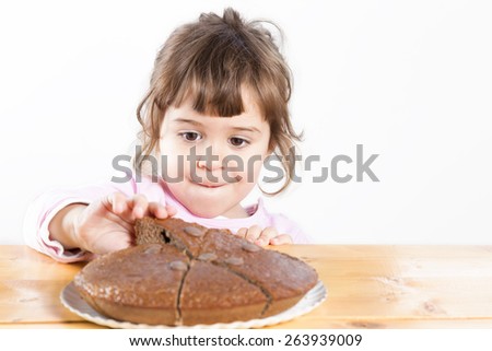 Little girl taking homemade chocolate cake. Concept of treat and temptation food. Cute toddler picking up a piece of delicious cake