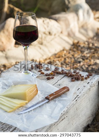 Pieces of cheese and raisins with a red wine glass on a old wooden board in the countryside. A rustic lunch with Idiazabal cheese cut and wine
