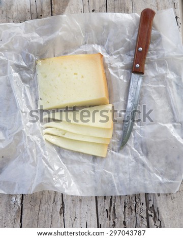 Pieces of cheese with with a knife on a old wooden board in the countryside. A rustic lunch with Idiazabal cheese