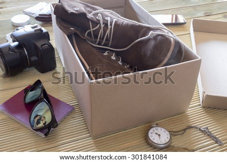Open box with a pair of boots. Couple giving a kiss to an adventure trip. Reflection on sunglasses of couple saying goodbye. Variaty of utensils to travel.