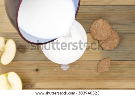 Saucepan pouring hot milk to splash in bowl to breakfast. Healthy breakfast of milk heated in fire without use microwave with cut apple and biscuits