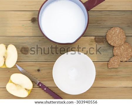 Saucepan with hot milk and bowl to breakfast . Healthy breakfast of milk heated in fire without use microwave with cut apple and biscuits