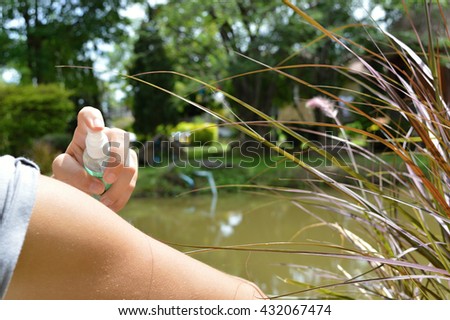 Woman spraying mosquito repellent on skin while sitting at a lake